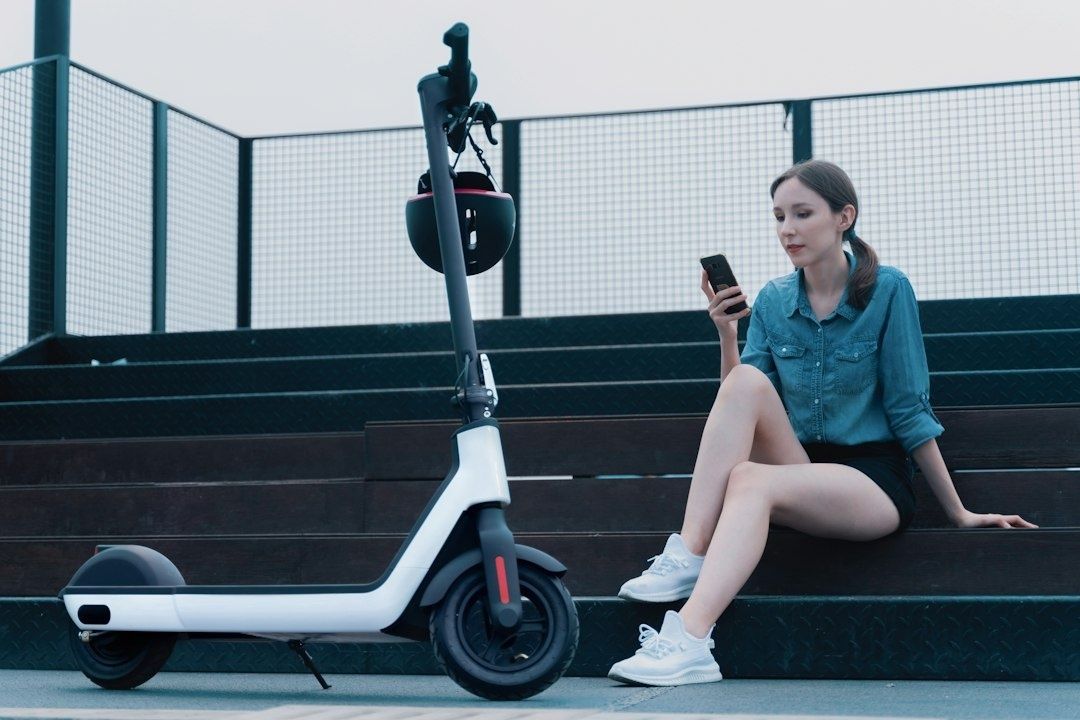Kvinna använder mobilen bredvid en parkerad elsparkcykel